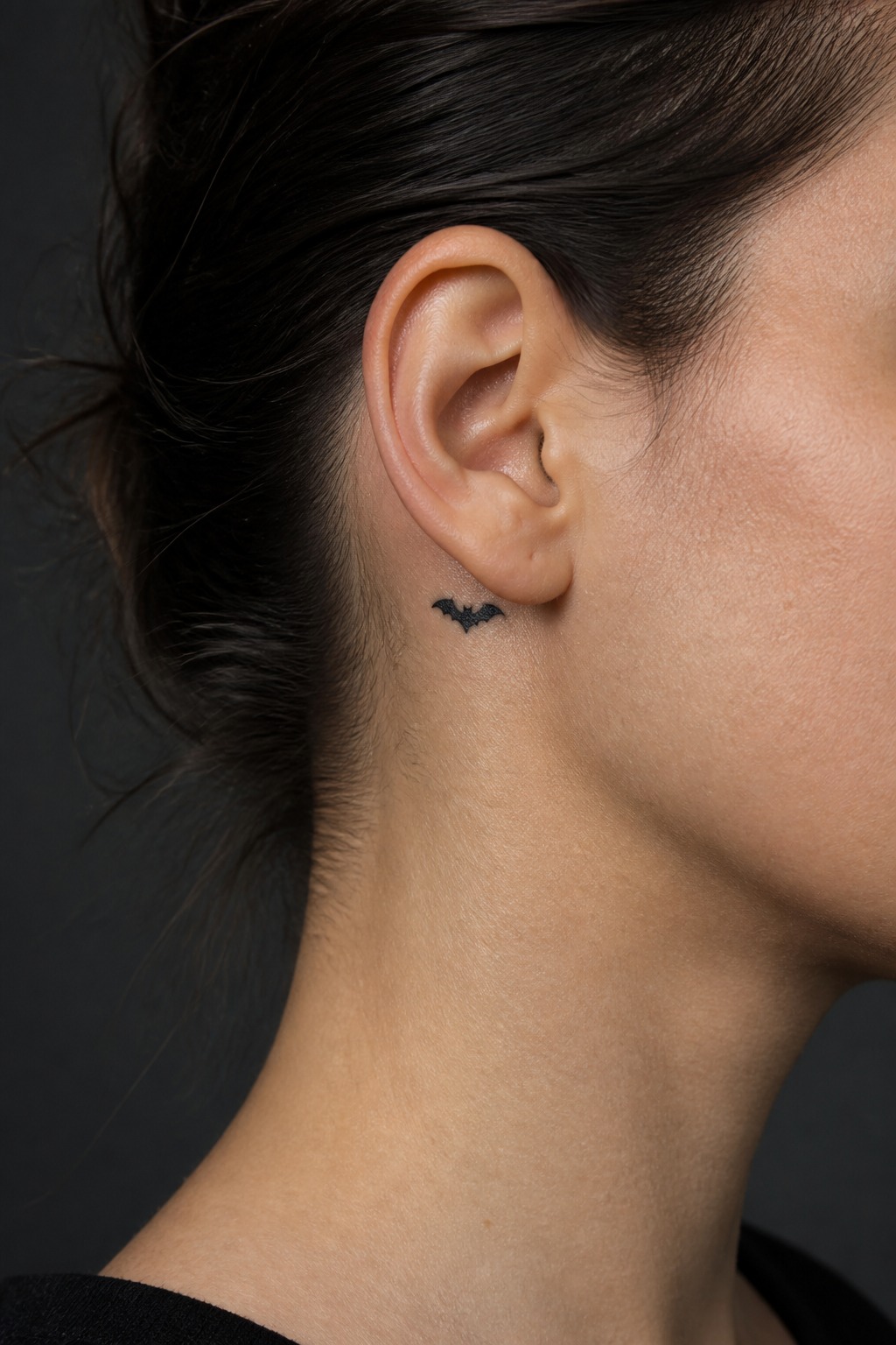 Minimalist bat silhouette behind the ear tattoo